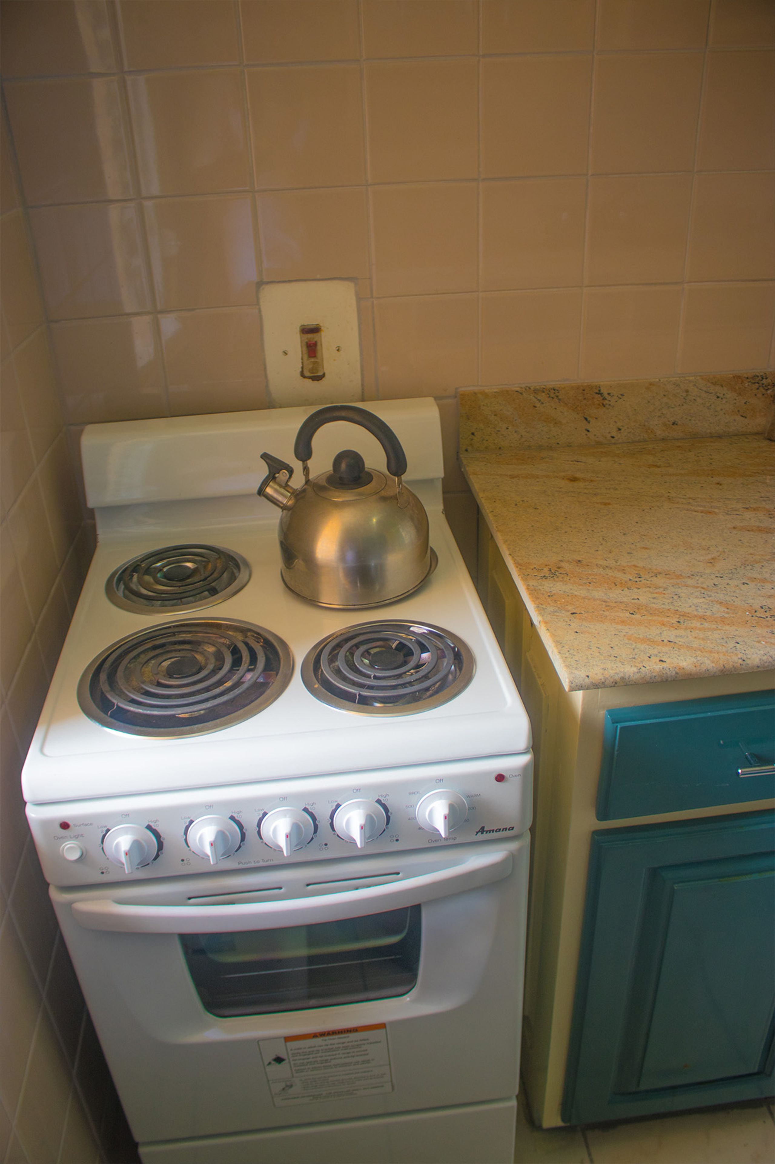 A kitchen with a white stove, a kettle, and teal cabinets.