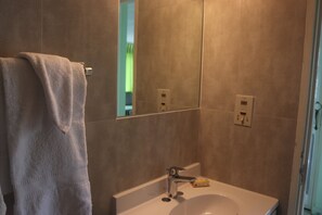 A bathroom with a white sink, a towel hanging on a rack, and a mirror reflecting a green wall.