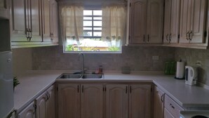 Una cocina con armarios de madera, un lavamanos doble y un ventanal con cortinas.