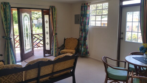 A room with a wooden bed, a chair, a table with a vase, and a window with curtains. - 3 Angels (Bridgetown)