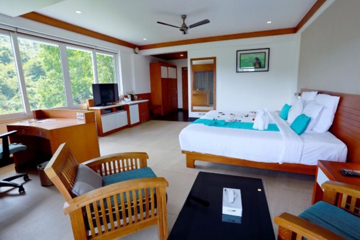Habitación de hotel con cama, escritorio, sillas, televisor y ventanas amplias.