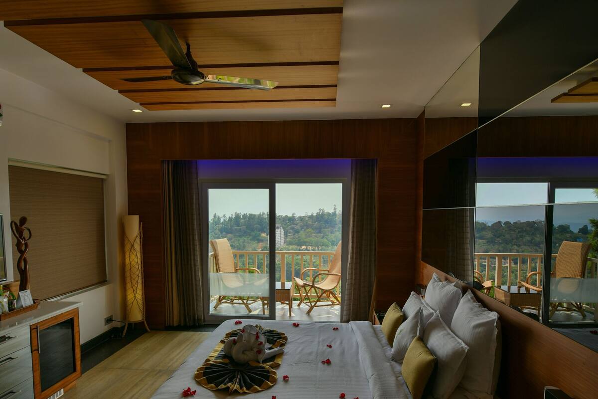 A hotel room with a large bed, a desk, a television, and a balcony with a view.