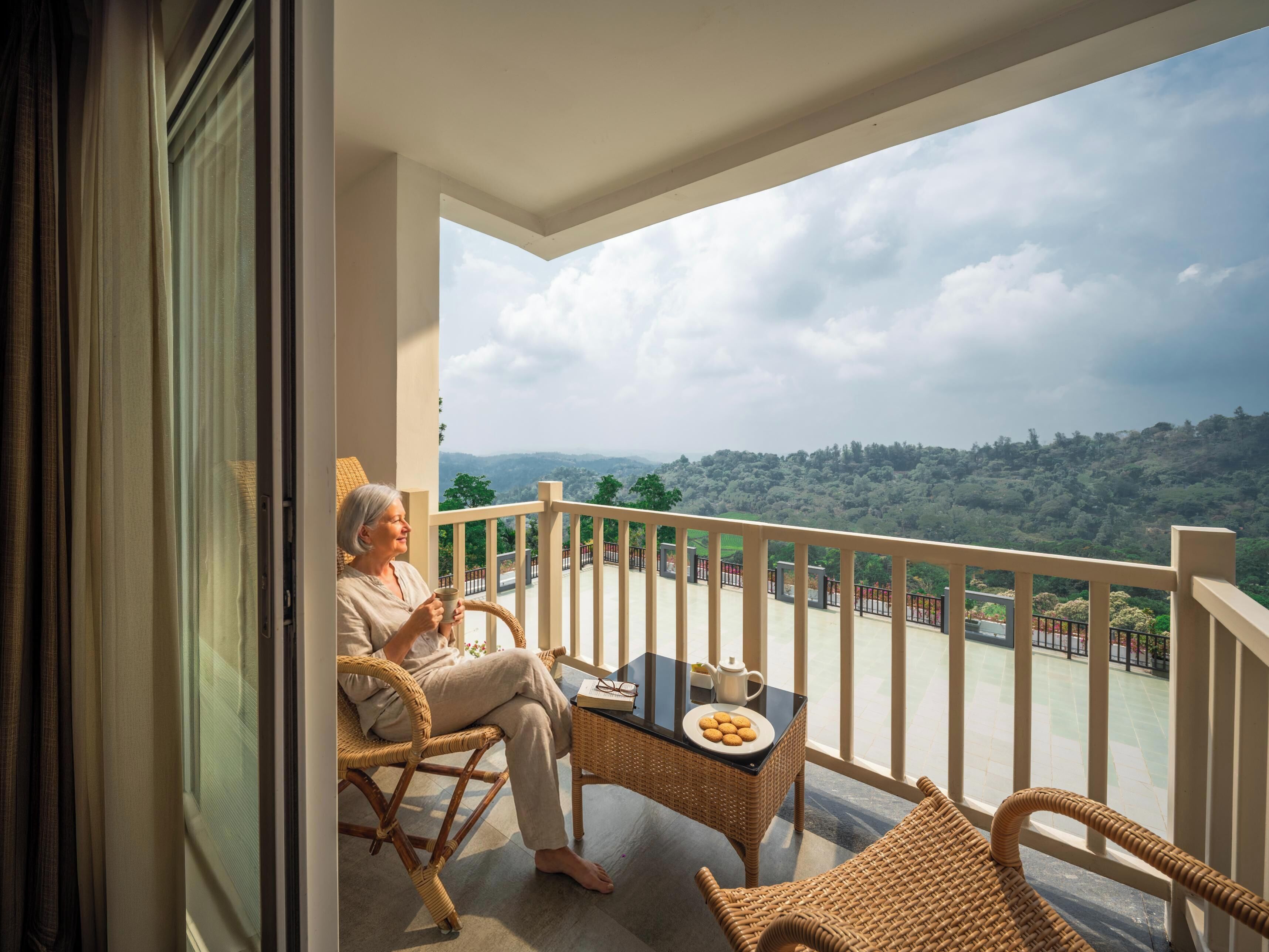 A balcony with a view of a hilly landscape, wicker furniture, and a table with a plate of cookies.