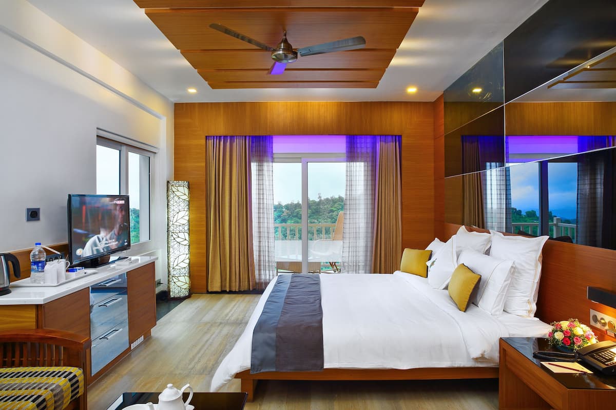A hotel room with a bed, a desk with a television, a balcony with curtains, and a ceiling fan.