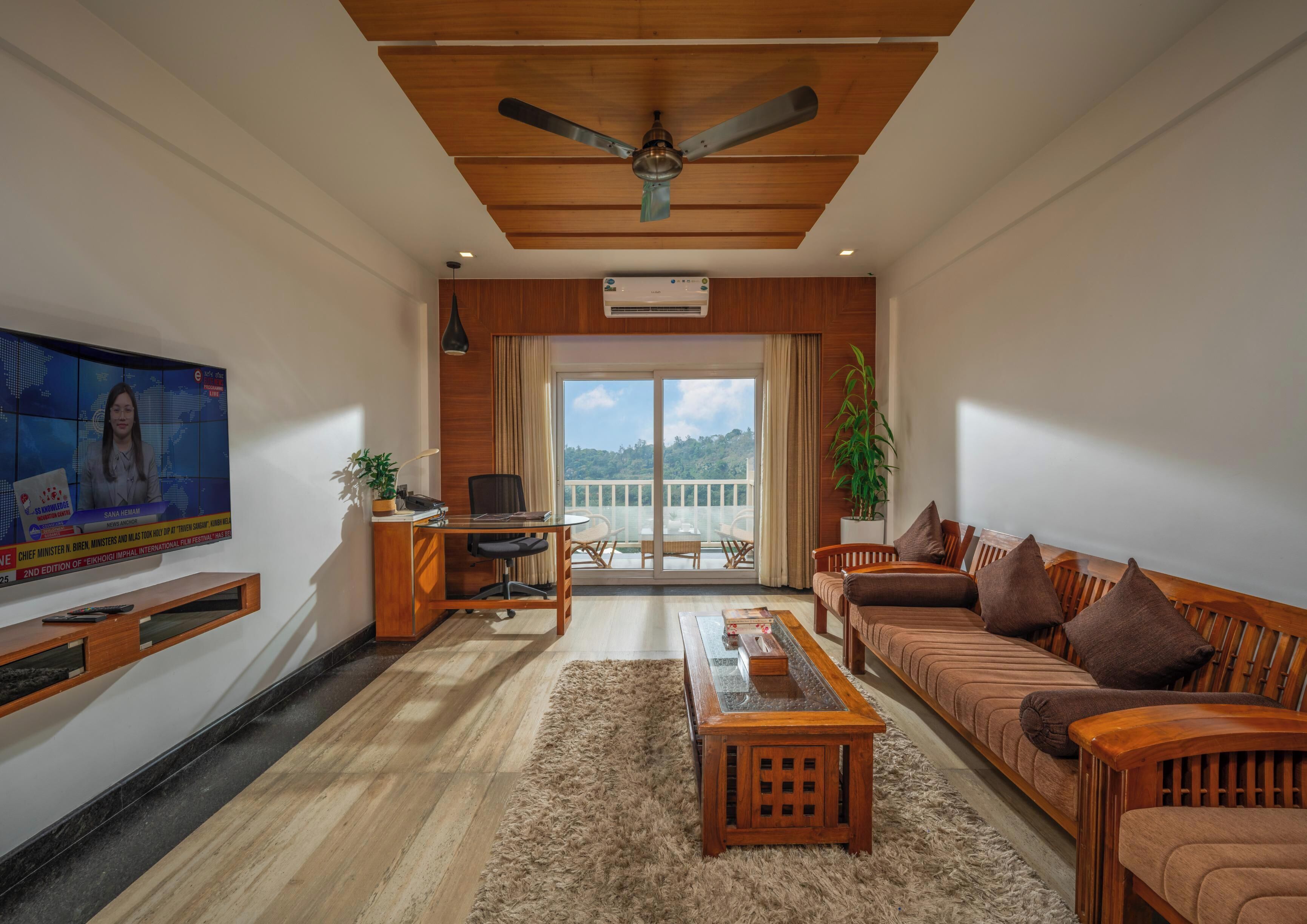 A modern living room with a wooden ceiling, a television, a desk with a chair, a sofa, and a balcony with a view.