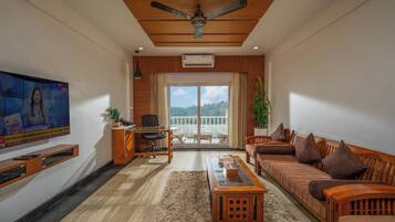 A modern living room with a wooden ceiling, a television, a desk with a chair, a sofa, and a balcony with a view.