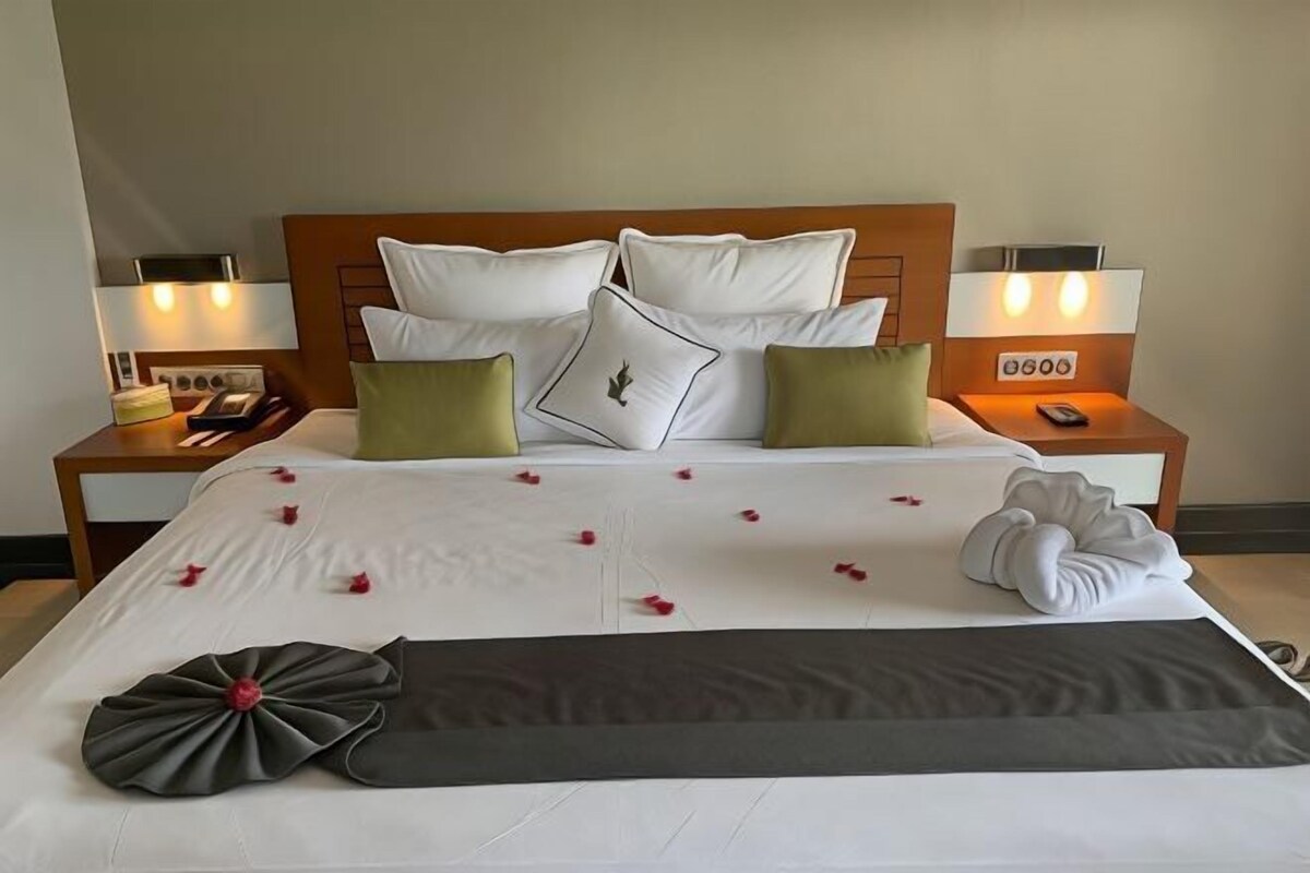 A hotel room with a neatly made bed, two bedside tables with lamps, a clock, and a telephone.