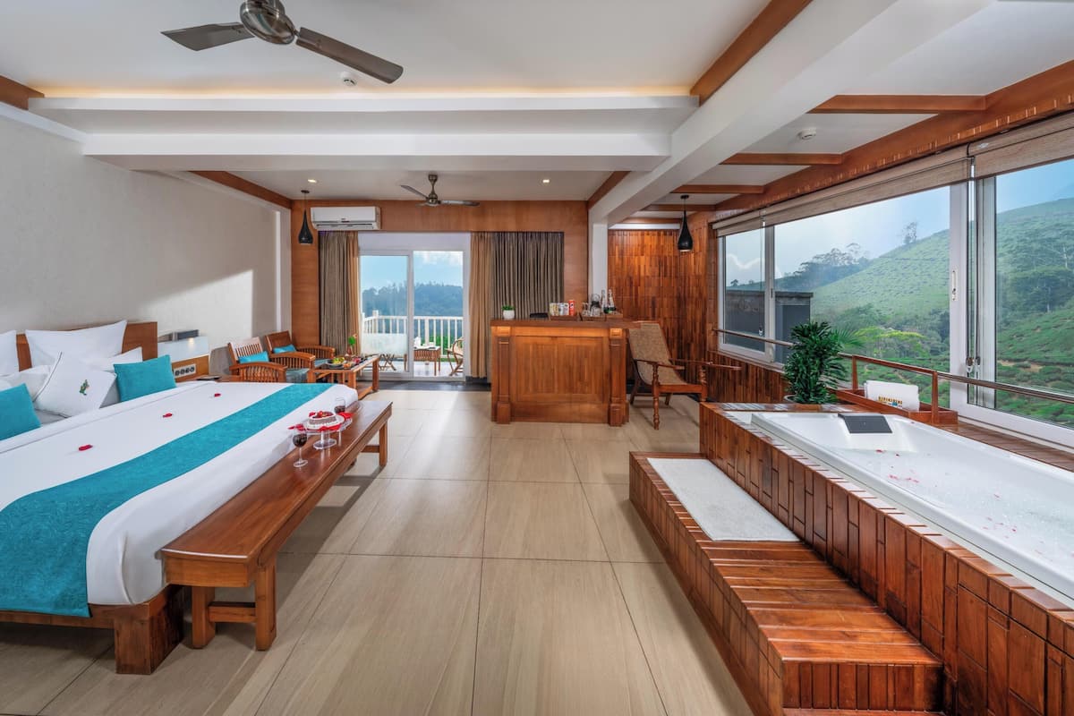 A modern hotel room with a large bed, a sitting area, a reception desk, and a bathtub.