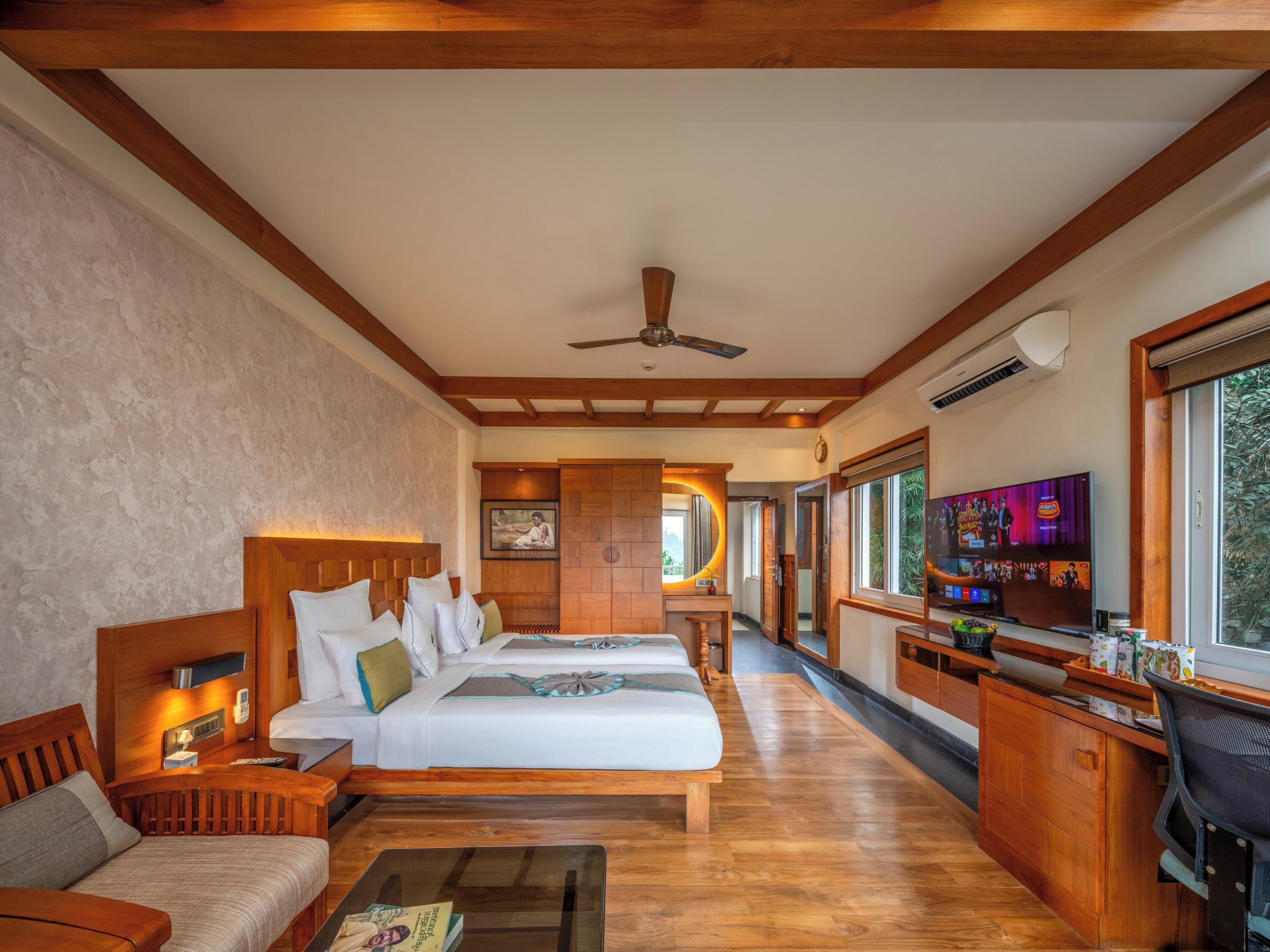 Una habitación de hotel con una cama, un sofá, un escritorio, un televisor y un ventilador de techo.