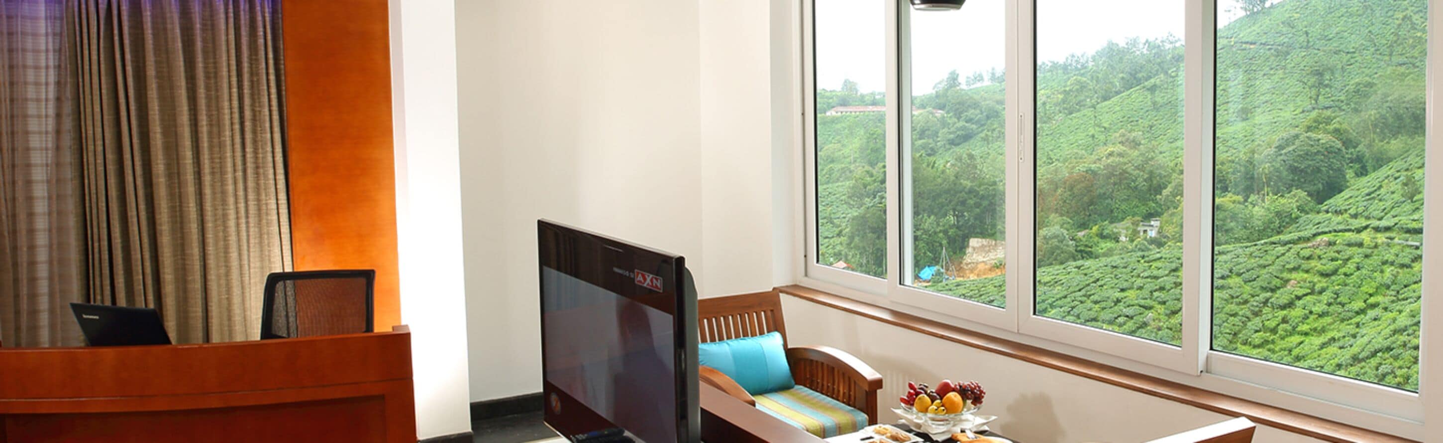 A hotel room with a large window offering a view of a lush green landscape.