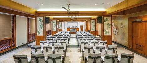 A conference room with rows of chairs, a podium, and a ceiling fan.
