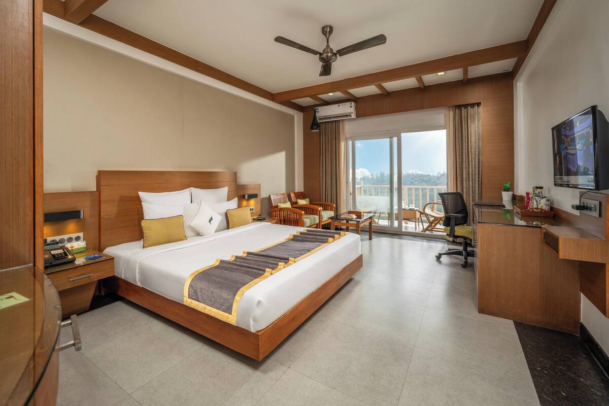 A hotel room with a large bed, a desk, a chair, a television, and a balcony with a view.