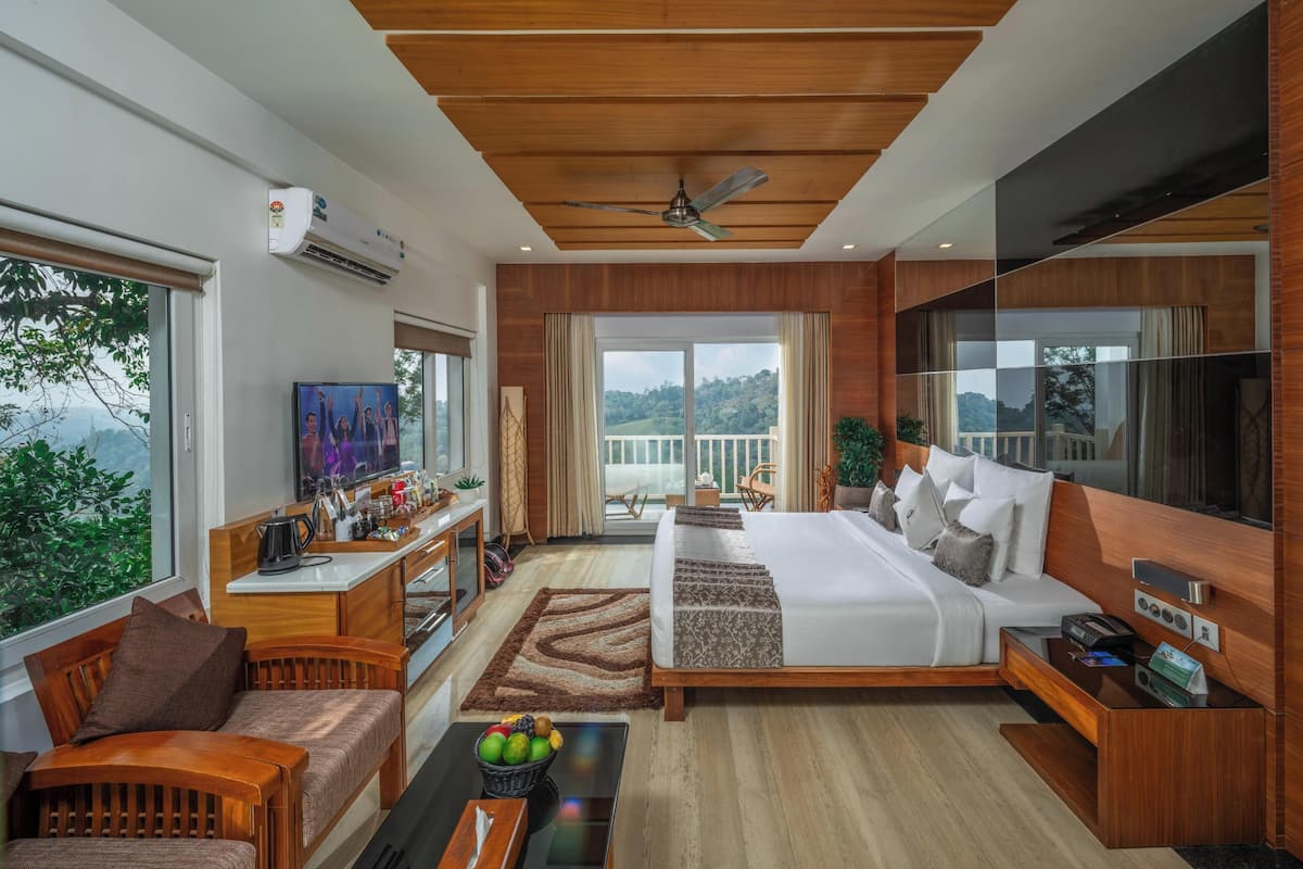 A modern bedroom with a large bed, a desk, a TV, and a balcony with a view.