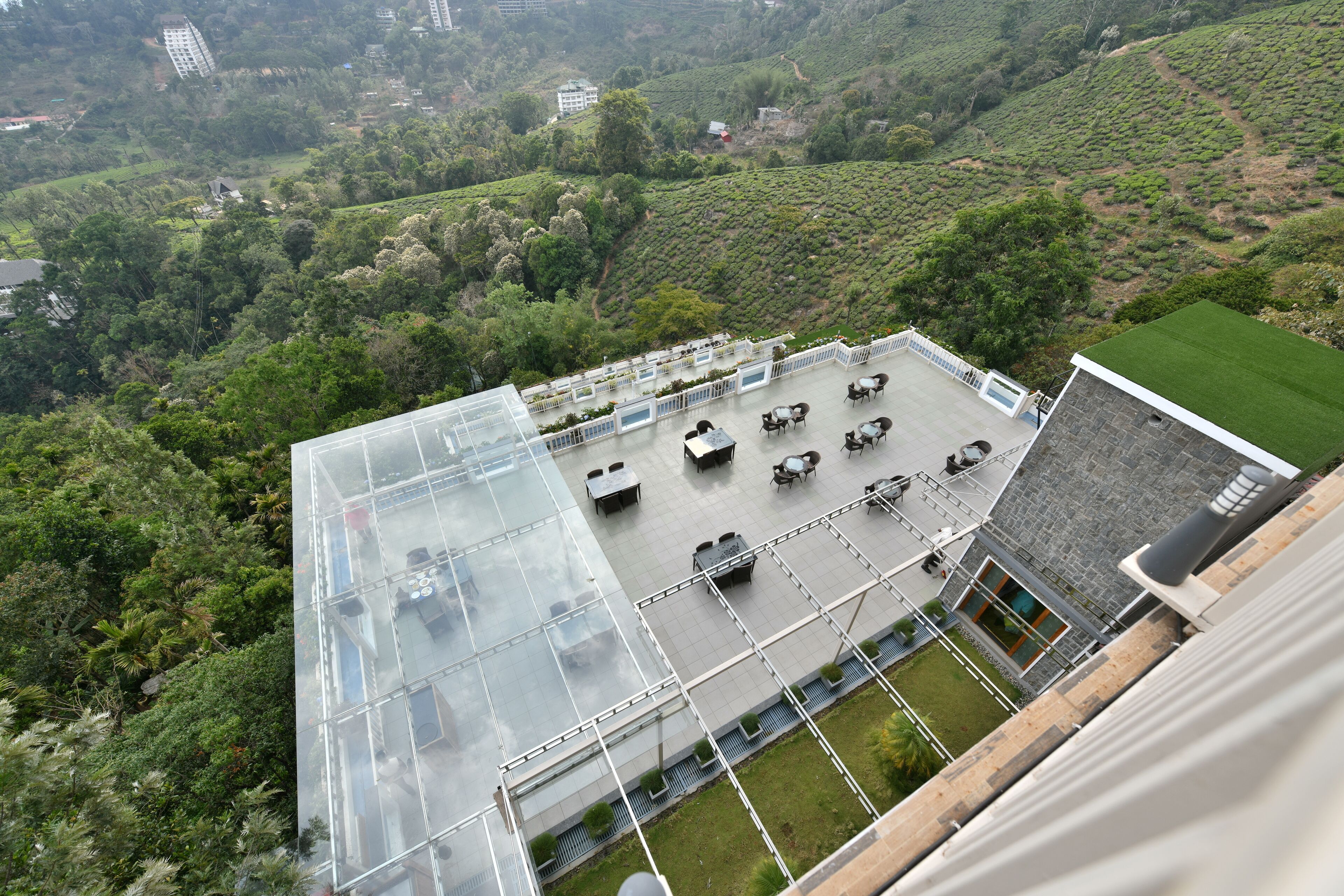 Una terraza en la azotea con mobiliario exterior, un invernadero de cristal y vistas a la vegetación circundante.