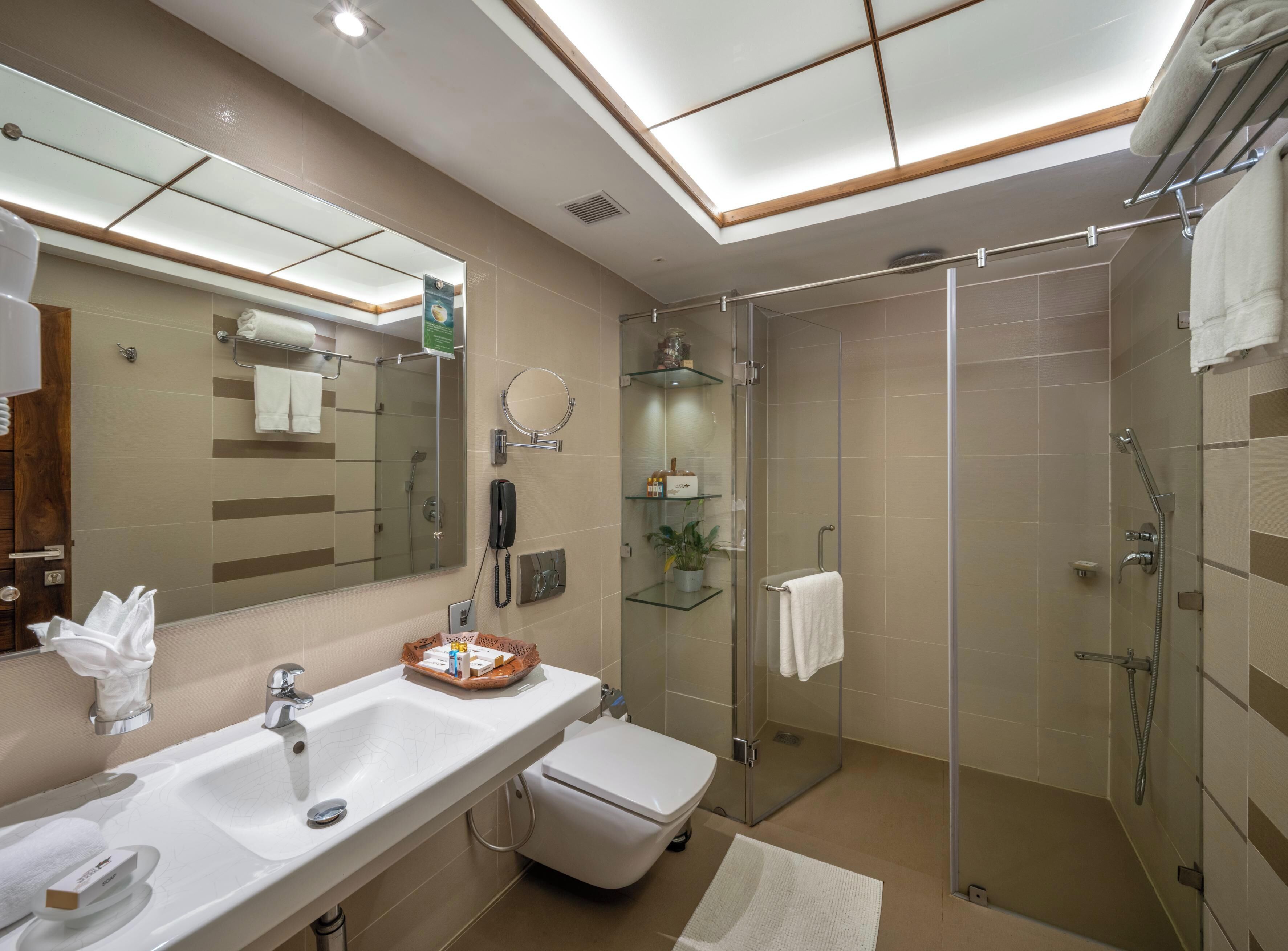 Un baño moderno con ducha envuelta en vidrio, un espejo grande y un lavabo con toallero.