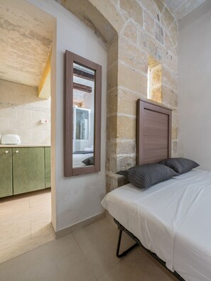 A bedroom with a stone wall, a wooden headboard, a bed with white bedding, and a green cabinet. - Valletta Holiday Old Theatre Lane (Valletta)