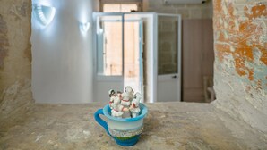 Un interno rustico con pareti in mattoni a vista, una tazza di ceramica blu con figurini e una porta che dà su una stanza più luminosa.