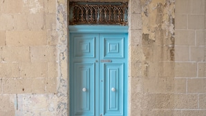 Una porta blu con un elemento decorativo in metallo nella parte superiore, incassata in un muro consumato dal tempo con segni di usura e un piccolo gradino che vi conduce.