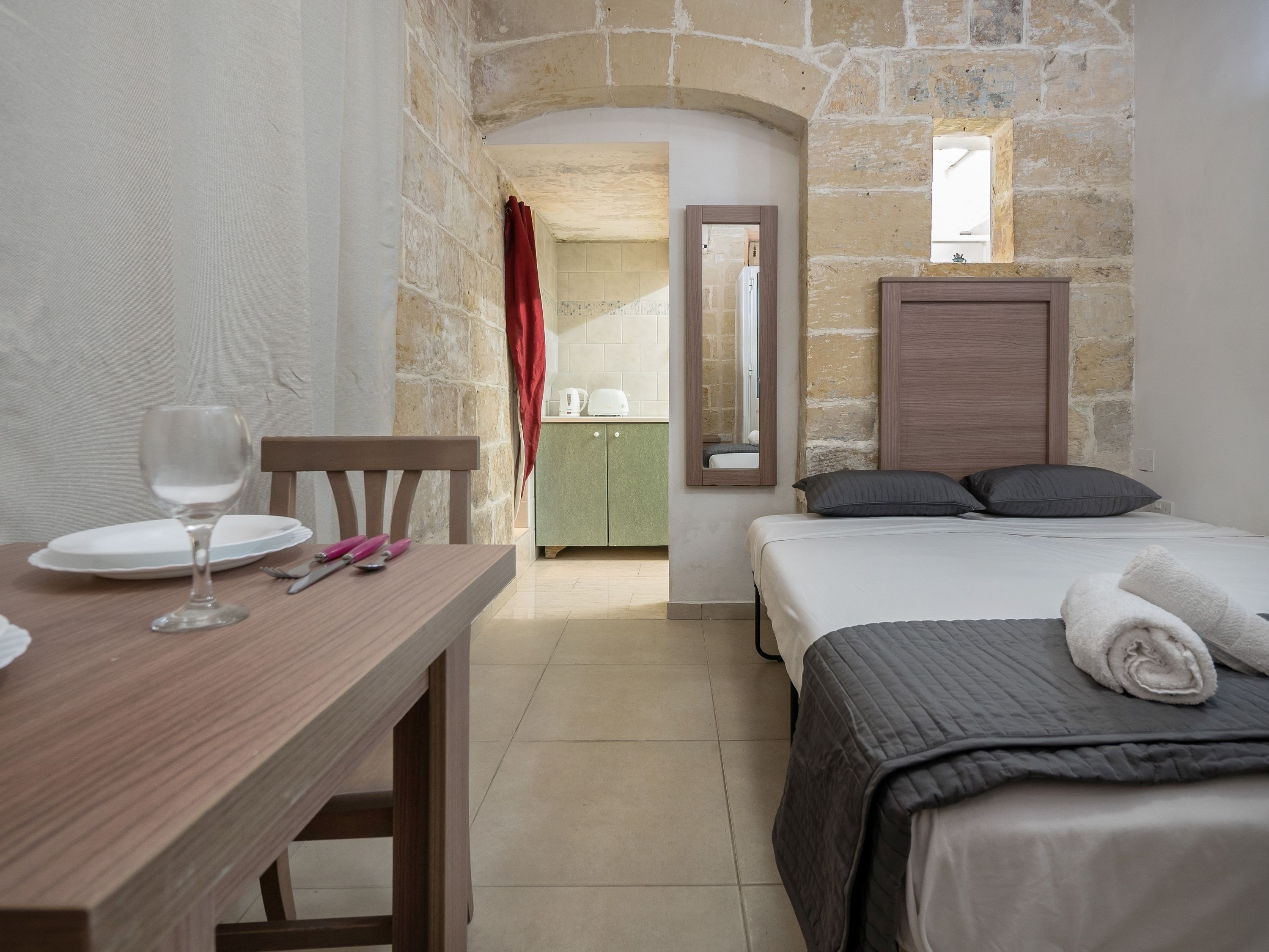 A bedroom with a bed, a wooden table with a wine glass, and a green cabinet.