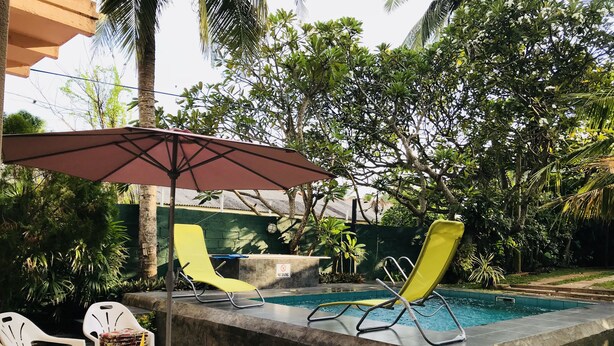 A swimming pool with two yellow lounge chairs and a red umbrella.