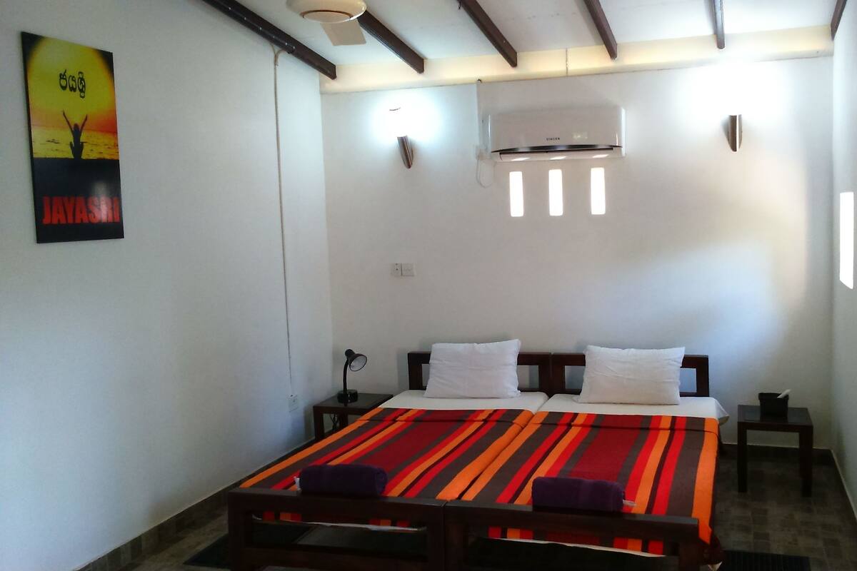 A room with a bed, two bedside tables, a wall-mounted air conditioner, and a poster on the wall.