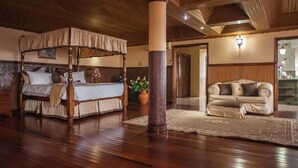 A spacious room with a four-poster bed, a sitting area with a sofa, and a large pillar. - Clarridge Hall Guesthouse (Montego Bay)