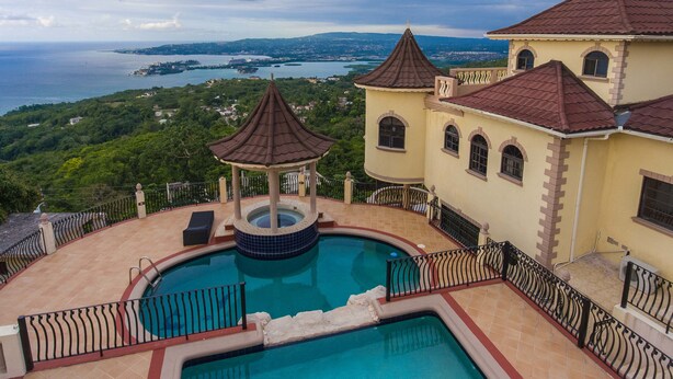 A pool area with a gazebo, a view of the sea, and a building with a red roof. - Clarridge Hall Guesthouse (Montego Bay)