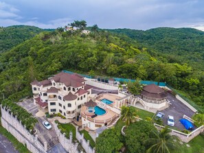 A large, multi-story resort with a swimming pool, multiple balconies, and a view of lush green hills.