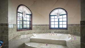 A bathroom with a freestanding bathtub, two arched windows with curtains, and a tiled floor. - Clarridge Hall Guesthouse (Montego Bay)