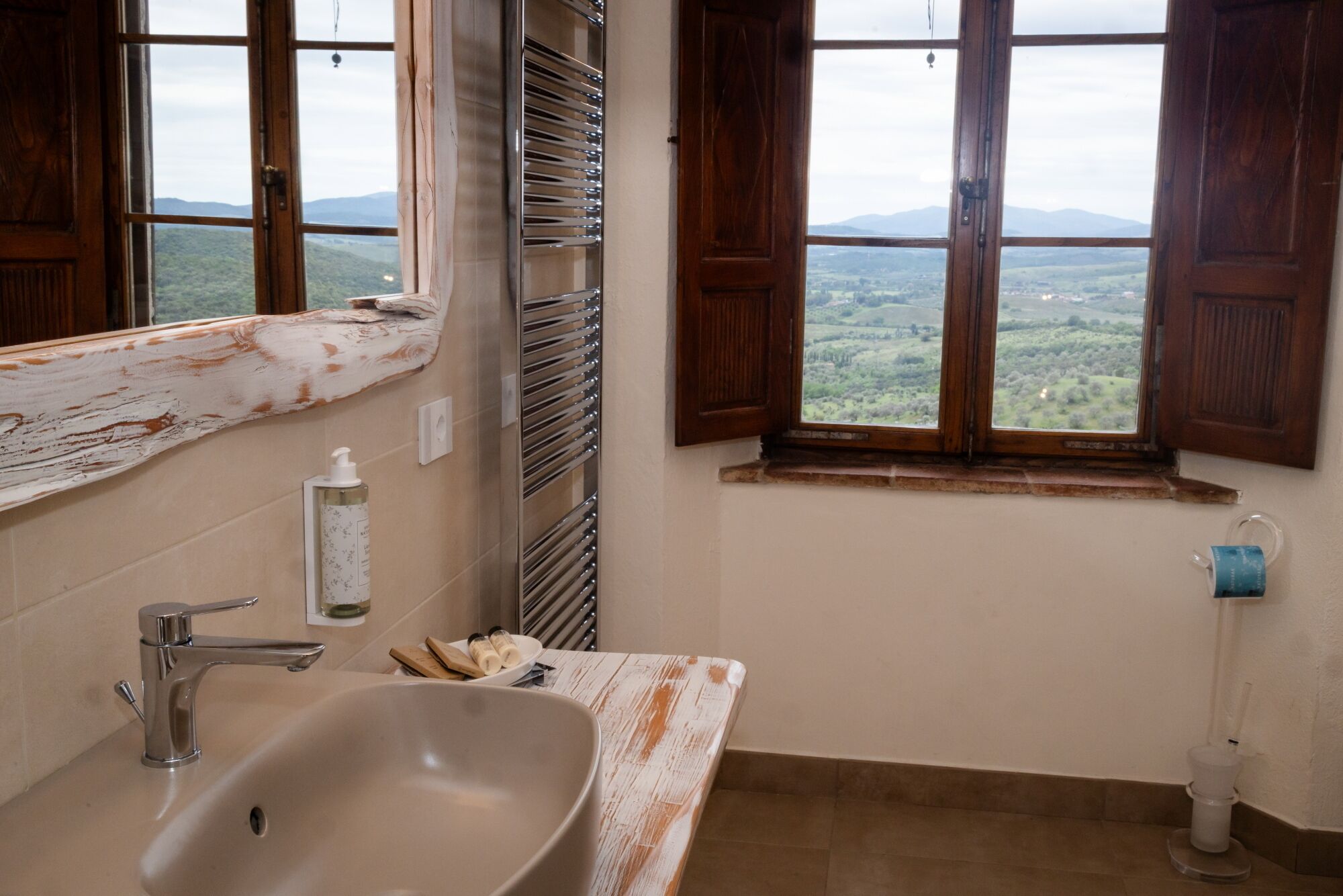A bathroom with a sink, mirror, and window with a view of a landscape.
