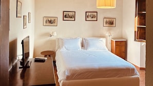 A bedroom with a large bed, wooden beams, a TV, and framed pictures on the wall. - Agriturismo Tenuta di Montemassi La Fattoria (Roccastrada)