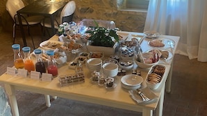 A breakfast buffet with various food items and beverages, set in a room with stone walls and a large window. - Agriturismo Tenuta di Montemassi La Fattoria (Roccastrada)