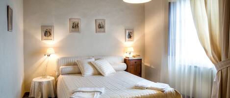 A hotel room with a large bed, two bedside tables, a lamp, and a window with curtains.