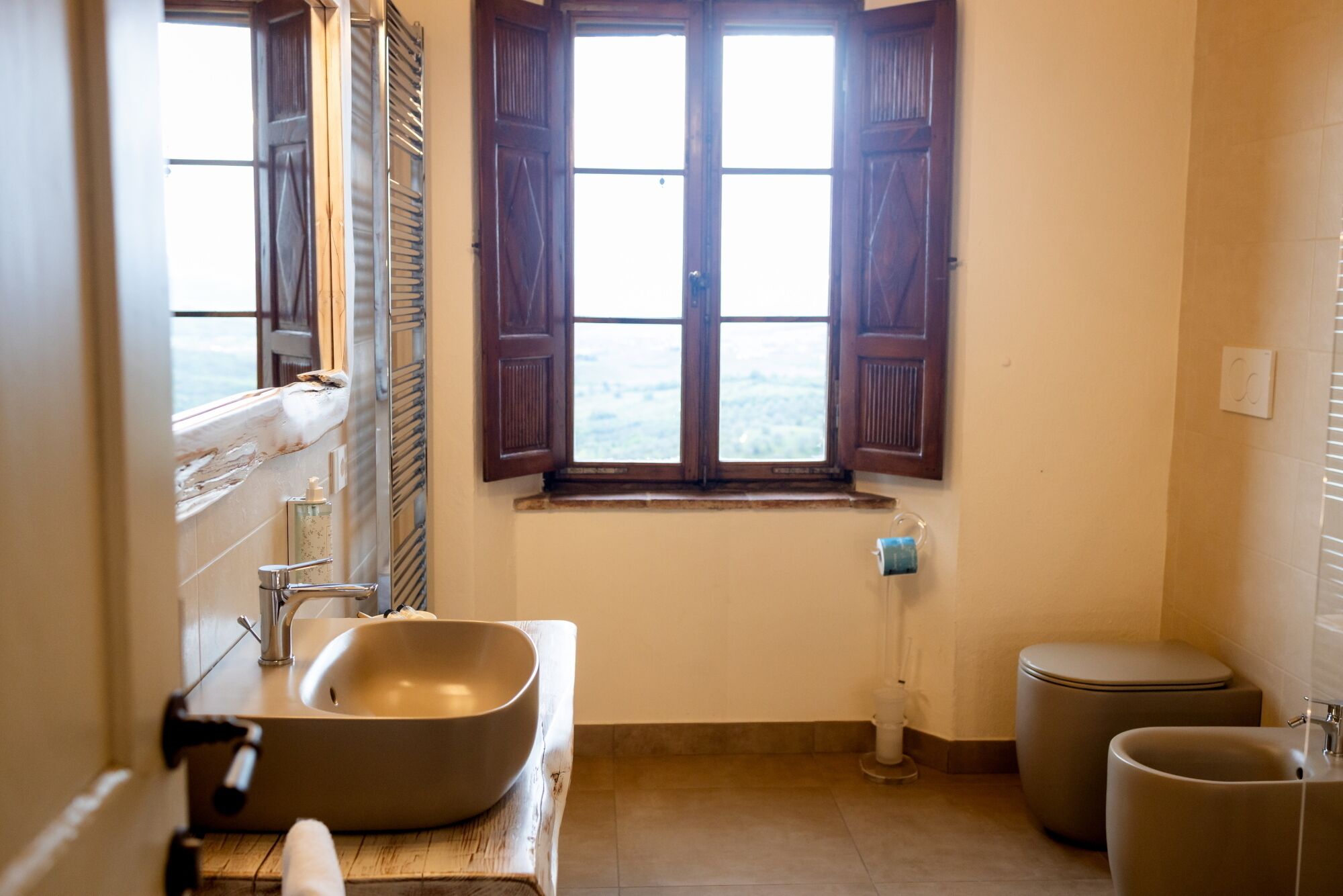 A bathroom with a large sink, a mirror, a window with wooden shutters, and a toilet.