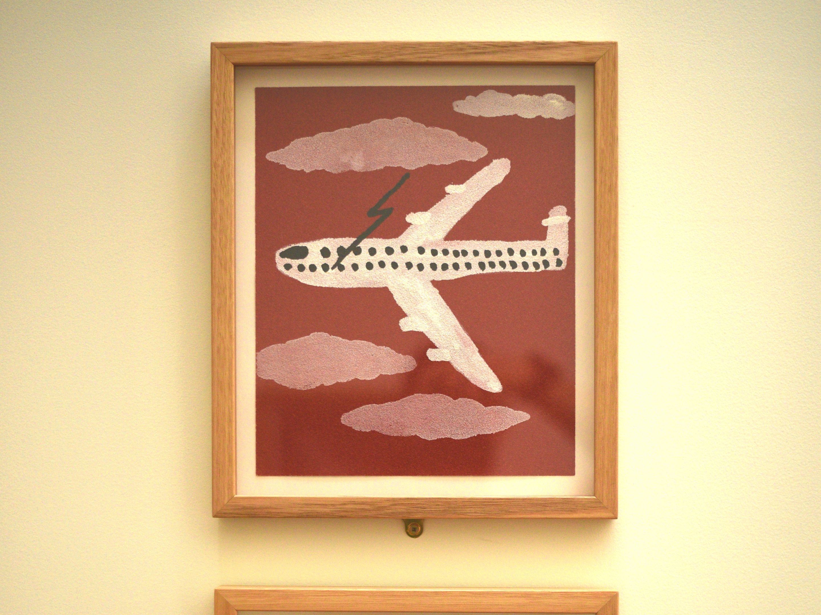 A framed artwork of an airplane with clouds and a lightning bolt on a red background.