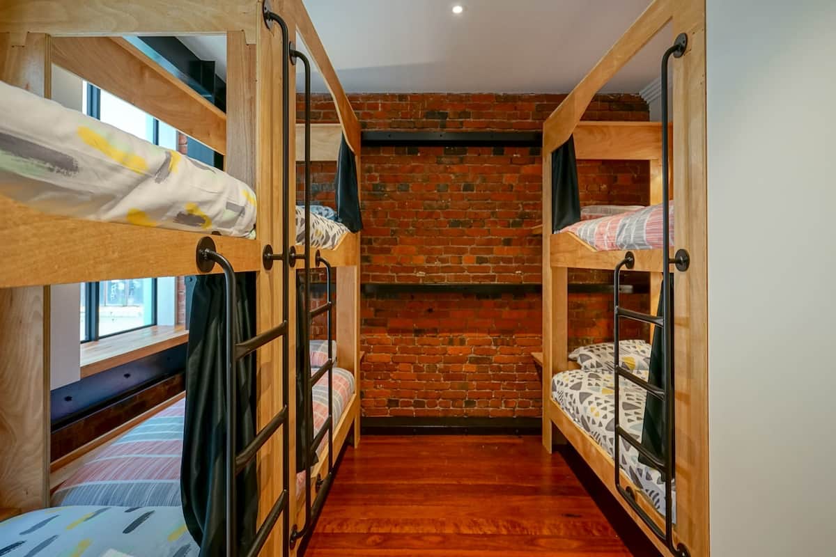 A room with three bunk beds, a brick wall, and a wooden floor.
