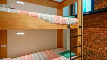 A bunk bed with a wooden headboard, a lower bunk with a plaid blanket, and a brick wall.