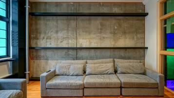 A modern living room with a grey sectional sofa, a wooden floor, and a concrete accent wall.