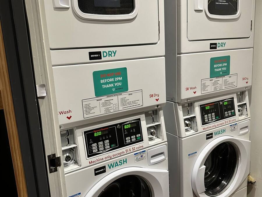 A row of stacked laundry machines with labels indicating 'Dryer 1', 'Dryer 2', 'Washer 1', and 'Washer 2'. Each machine has a digital display and instructions for use.