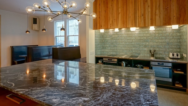 A modern kitchen with a marble island, wooden cabinets, and a backsplash. - The Marion Hostel (Wellington)