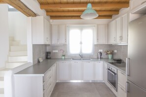 Una cocina moderna con armarios blancos, un refrigerador de acero inoxidable y techo de madera.