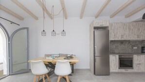 A modern kitchen with wooden beams, a dining table with chairs, and a refrigerator. - Salinus Villas (Naxos)