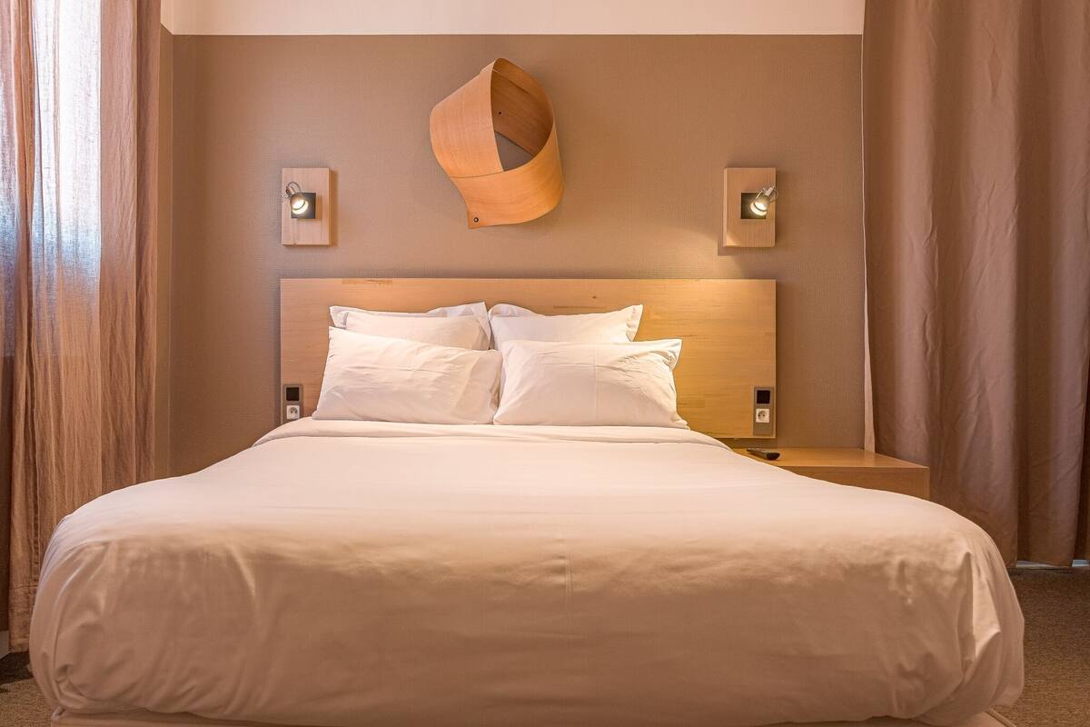 A hotel room with a large bed, wooden headboard, two bedside tables, and wall-mounted light fixtures.