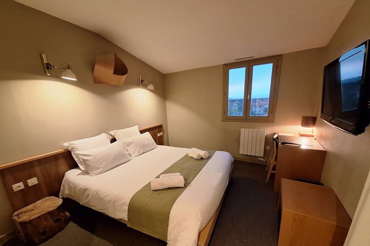 A hotel room with a bed, bedside table, lamp, and a TV mounted on the wall.