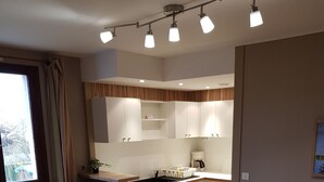 A modern kitchen with white cabinets, a dining area with a wooden table and chairs, and a built-in TV. - Résidence l'Atelier (Ennezat)