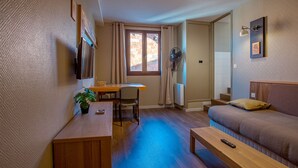A compact living space with a wooden dining table, a sofa, a small wooden bench, and a single bed. - Résidence l'Atelier (Ennezat)