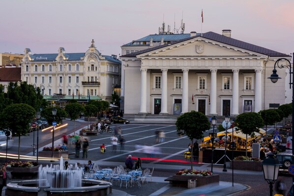 A public square with a fountain, outdoor seating, and a large building with columns.