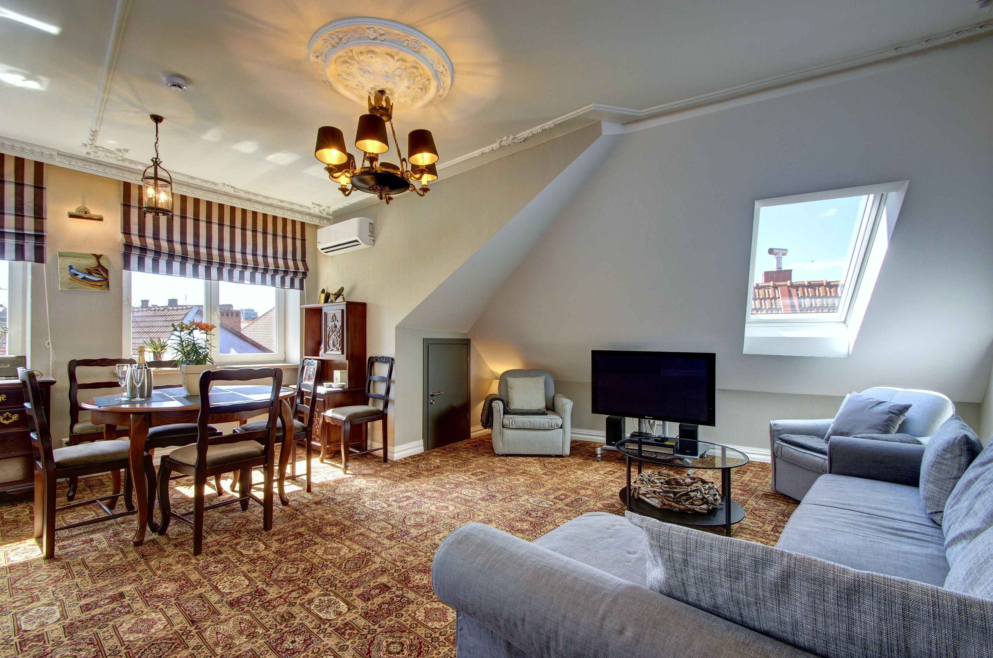 A living room with a television, a sofa, a dining area with chairs, and a patterned carpet.