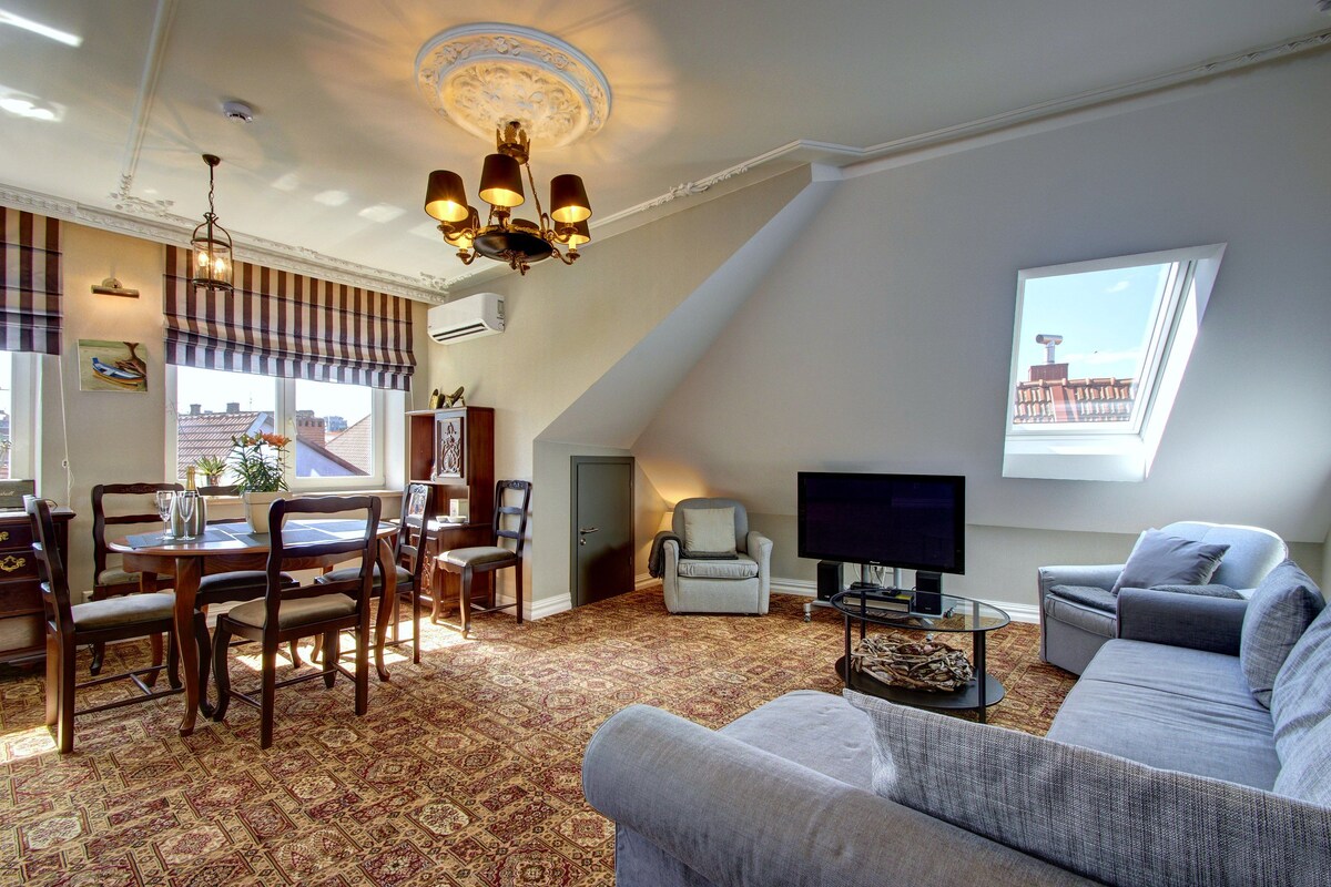 A living room with a television, a sofa, a dining area with chairs, and a patterned carpet.