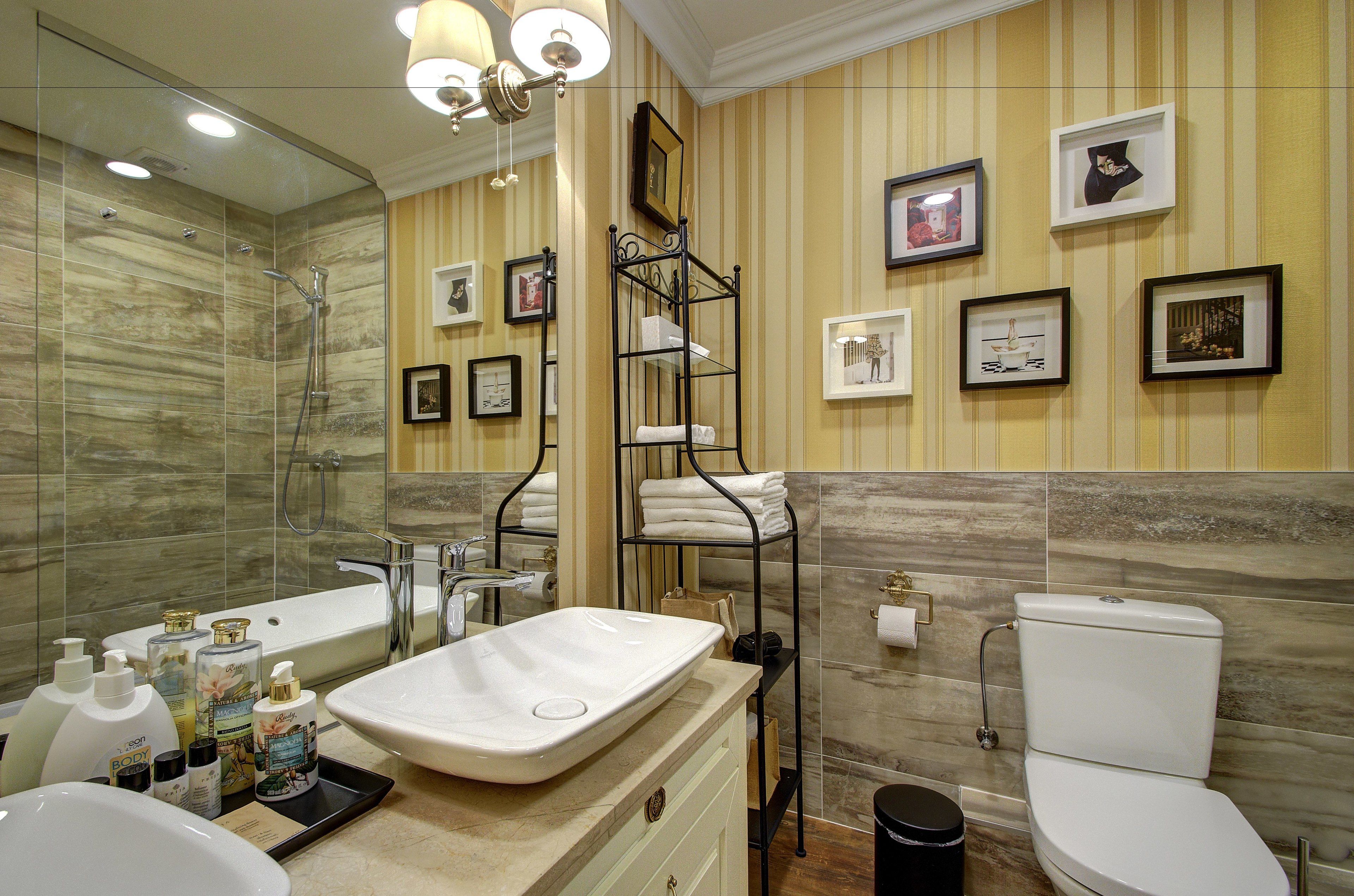 A modern bathroom with a bathtub, a sink, a toilet, and a shower. There are framed pictures on the wall and a shelf with towels.
